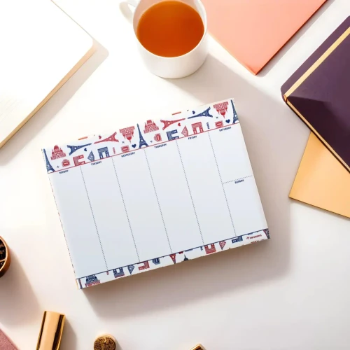 A paper weekly pad illustrated with red and blue drawings of Paris monuments, on a desk next to a cup of tea and documents.