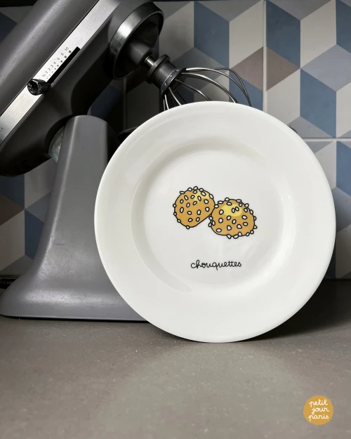 A white dessert plate with a French pastry illustration (chouquettes).