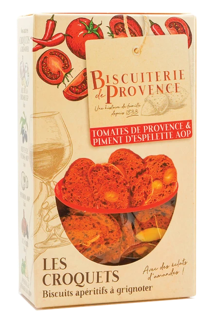 A 90 gram box of organic croquets with tomato and Espelette pepper from Biscuiterie de Provence. The crisp, red crackers with almond pieces are visible through the box's window.