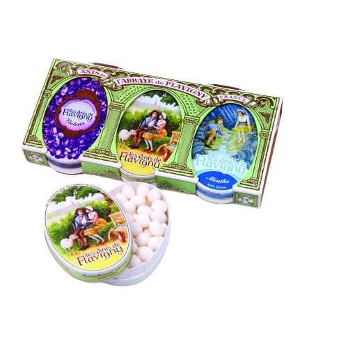 A box displaying three tins of Anis de Flavigny mints, totaling 150 grams. From left to right: the violet tin, whose top is drawn covered with violet flowers; the original flavor, whose top has two people sitting together, looking into each other's eyes; and the mint flavor, whose top features two people sitting by a stream.