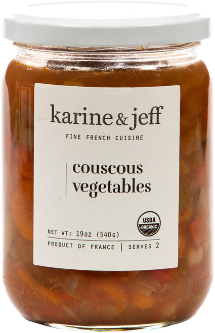 A 540 gram glass jar of organic couscous vegetables from Karine & Jeff. The carrots, zucchini, and other vegetables are chopped and suspended in a red sauce.