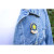 A magnetic brooch that reads "Rêve" pinned on a jean jacket. The brooch depicts a series of concentric stars changing from yellow to blue.
