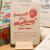 A "Fraise" card from L'Atelier Letterpress's "Excuse My French" series, displayed on a stand on a table. A sketch of strawberry is at the top of the card. Below it reads, 
"Bring back your strawberry! Ramène ta fraise! 'Ramène ta fraise' is a colorful French slang expression which often affectionately means "Come here!" When we speak of a person who "brings back her strawberry," it can also mean a person who has a pretentious or inappropriate attitude."