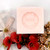 A 100 gram light peach colored cube of Senteurs de France's rose-scented Marseille cube sitting atop white lilies.