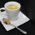 A brown Ercus croissant sugar piece sits on a spoon next to a latte.