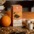 A box of Chevaliers d'Argouges dark chocolate tuile box with orange pieces sitting on a table next to an orange.