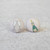 A pair of fabric button earrings from Rachel O's. One earring displays a cartoon drawing of two champagne glasses and the other a champagne bottle. The earrings are on a gray stone counter top.