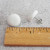 A close-up image of two white fabric button earrings next to a ruler. The fabric buttons are about half an inch wide with a half inch long butterfly back.
