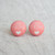 A pair of pink fabric button earrings with white text that says, "Je t'aime," with a white heart beneath it, from Rachel O's. The earrings are on a gray stone counter top.