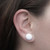 A close-up image of the ear of a person wearing a white fabric button earring.