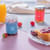 Two jars of jam on a table, next to orange juice and toast. One jam's label says "Super un an de plus!," while the other says, "Merci!"