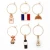 Six small wine charms attached to key rings, displayed in a three by two grid. The top row shows off the perfume, French flag, and croissant charms. The bottom row features the Moulin Rouge, wine bottle, and Eiffel tower designs.