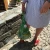 The lower half of a person in a dress, outside, holding a full large green cotton meshed shopping bag.