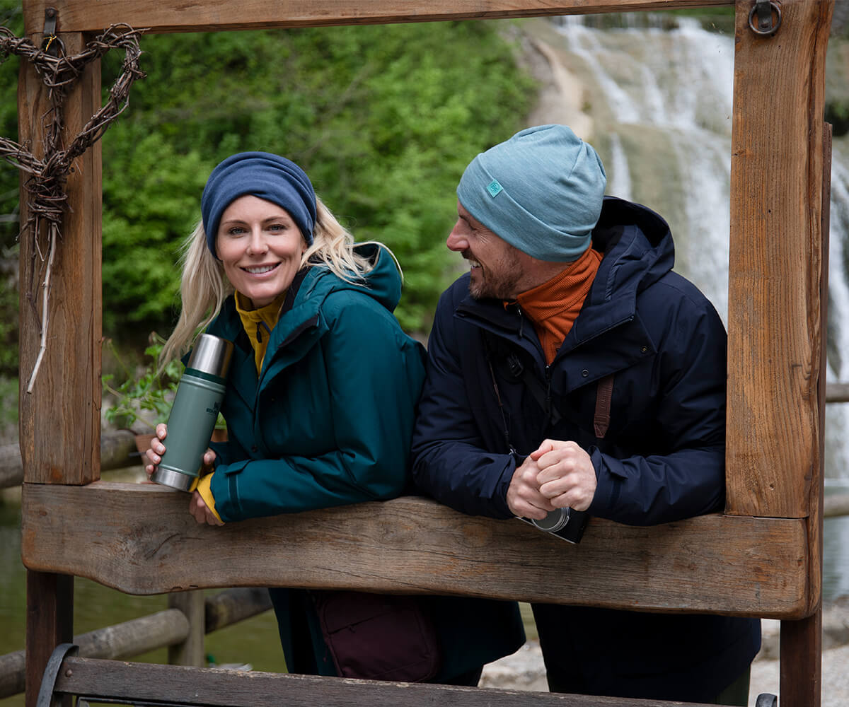Man and woman stood in front of waterfall, wearing new Bowland Jackets.