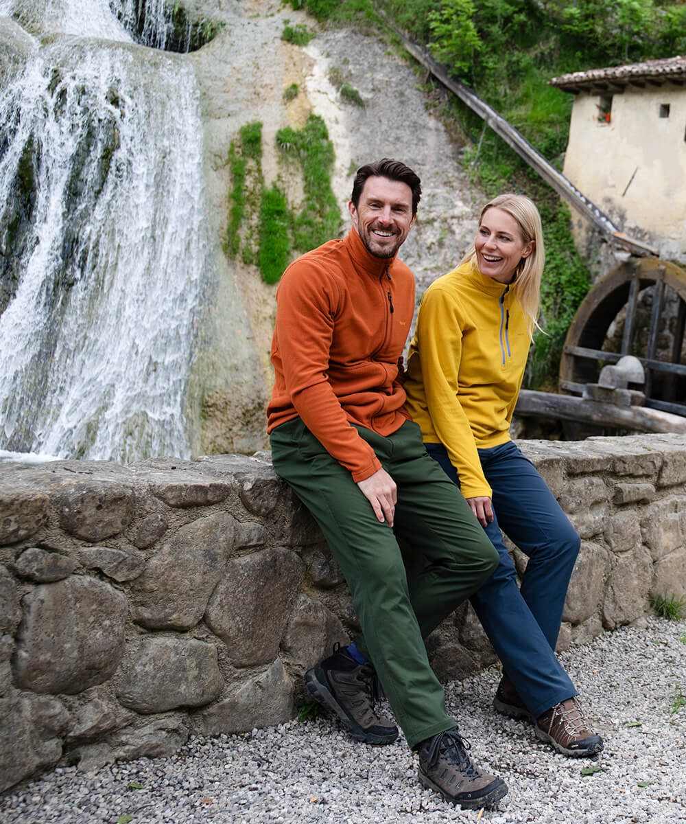 Man and woman sat on wall in front of waterfall, wearing bright coloured Microgrid Fleeces.