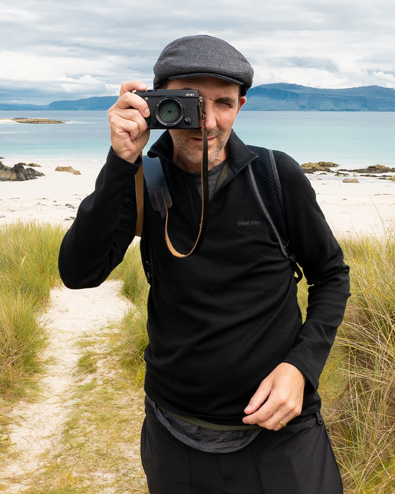 Chris Orange Holding a Camera, Stood in Front of Lake in Scotland