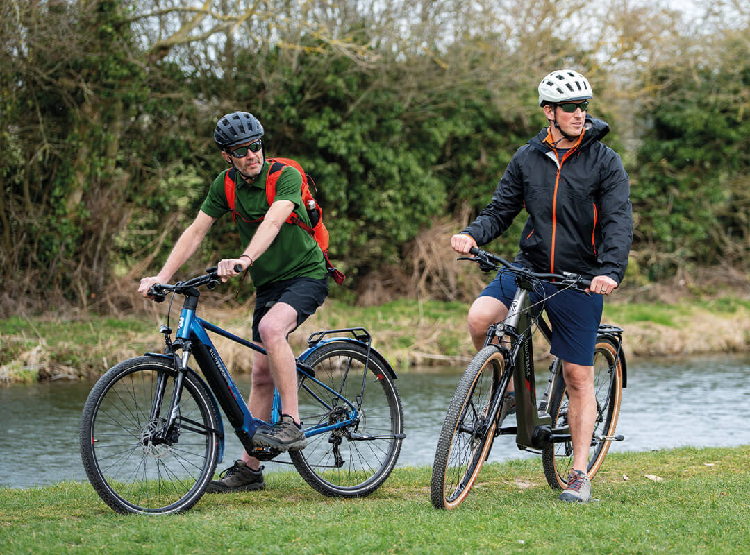 Two people stopped on their e-bikes, beside water