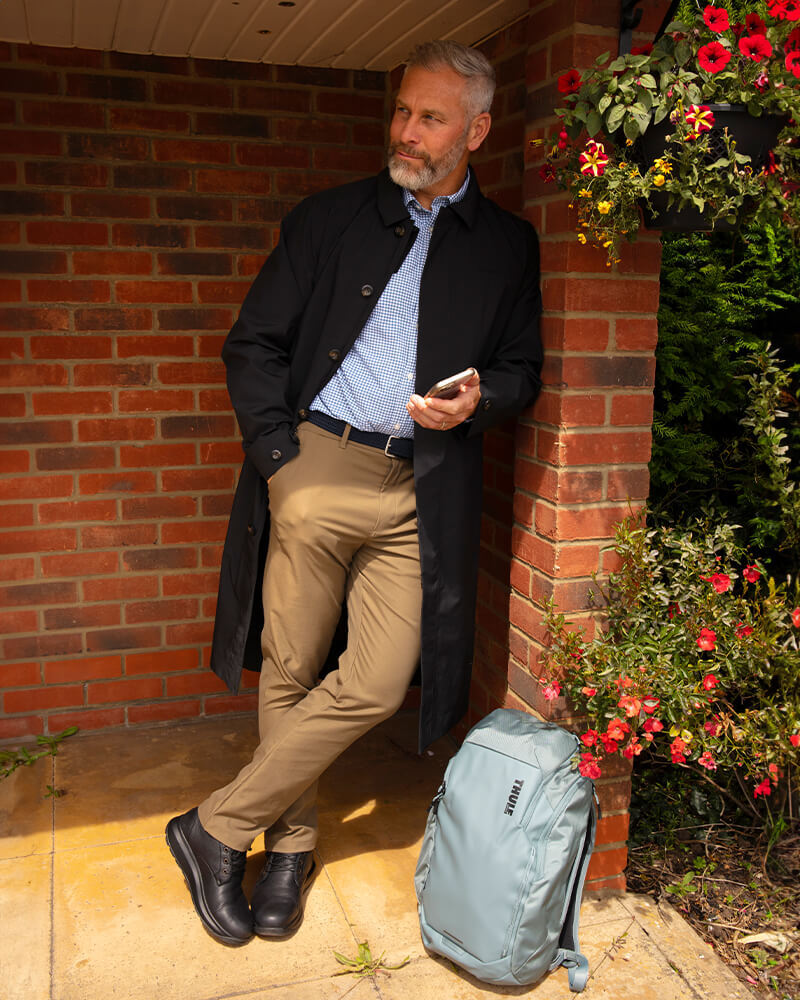 Man Dressed in Business Attire Standing at a Bus Stop with Thule Backpack