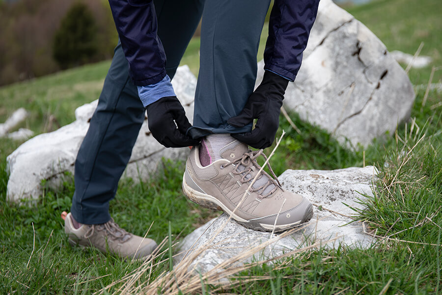 Woman adjusting shoes with one foot on a rock, wearing Oboz walking shoes