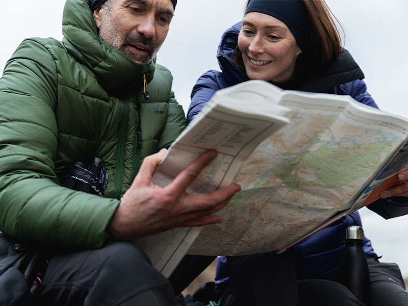 Man and woman reading a map, wearing insulated clothing on a winter walk.