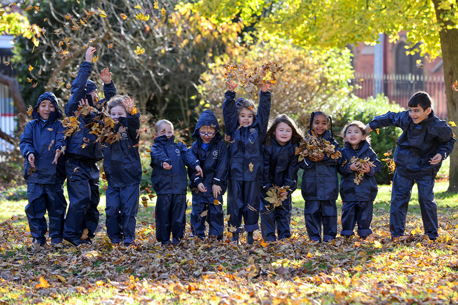 The Outdoor Guide Foundation - a group of children in waterproof clothing and wellies, playing in a patch of autumn fallen leaves