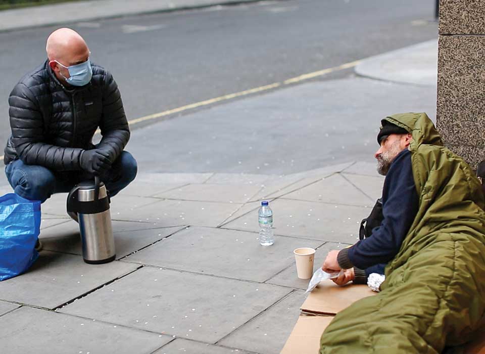 man talking to a homeless person on a street in a sleeping bag