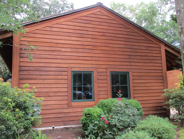 J.Racenstein Tabernacle Harvest Deck and Wood Stain DRP, close-up of a wooden barn exterior with horizontal stained wood siding and two window panes, surrounded by garden plants.