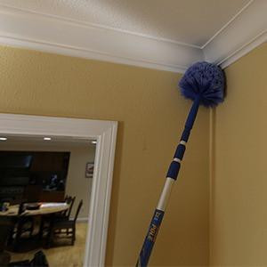 Ettore Brush Cobweb with click lock feature, dusting ceiling corners with a long-handled brush in a home interior.
