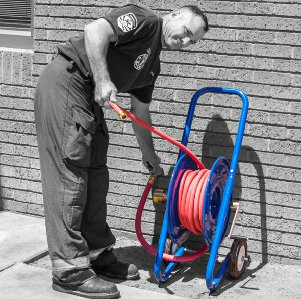 J.Racenstein Reel Dolly style 225/300ft 4000psi Cox, image of a man handling a hose reel on a blue cart outside against a brick wall.