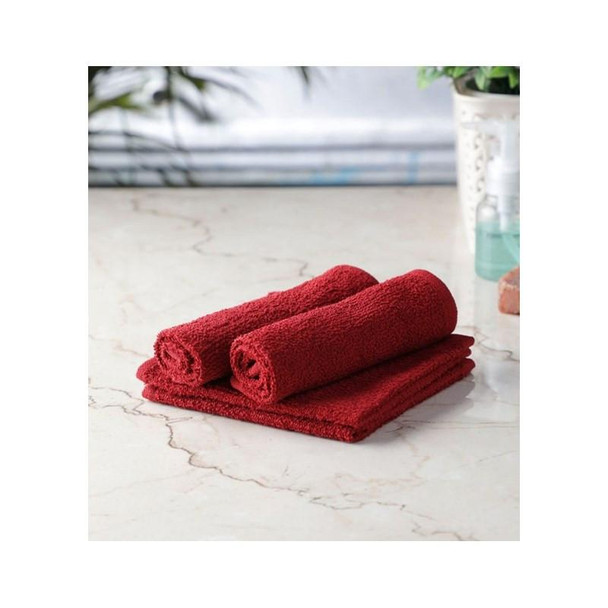 J.Racenstein Turkish Towels, three red towels neatly rolled and folded on a marble surface with a blurred background of a potted plant and bathroom accessories.