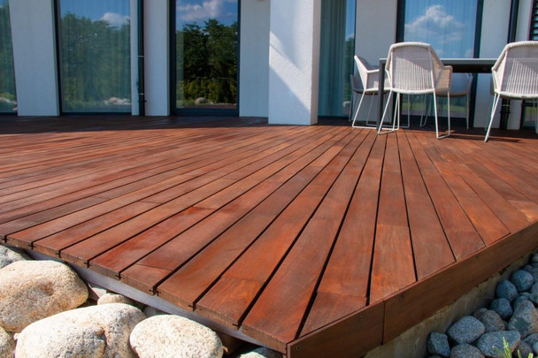 ProTool Protool Oxy Wood Cleaner, a wooden outdoor deck area with a clean, polished wood surface and surrounding rocks, sunlight, and outdoor furniture in the background.