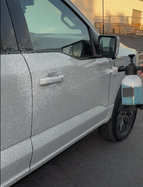ProTool Foamer Bottle Handheld Pump Up, person using it to spray foam on a silver car's door during car cleaning.