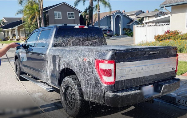 ProTool Foaming Hose End Sprayer, person using the sprayer to wash a black pickup truck with foam for cleaning outdoors in a residential neighborhood.