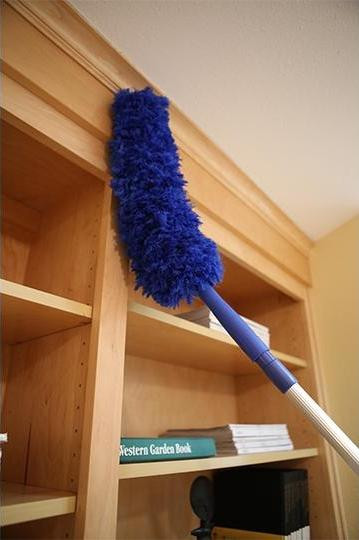 Ettore MicroSwipeDuster Ettore, blue microfiber dusting tool mounted on an extendable handle cleaning a wooden bookshelf.