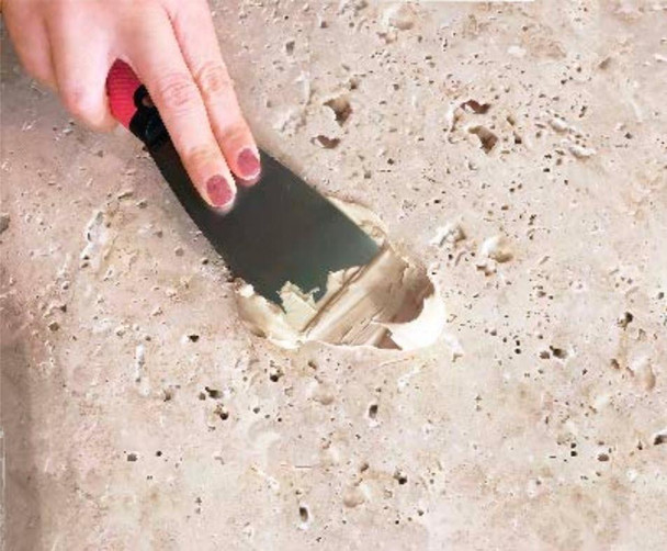 StonePro Traverfill Pro Adhesive Quart, hand applying beige adhesive to a stone surface with a notched trowel for tile and stone installation.