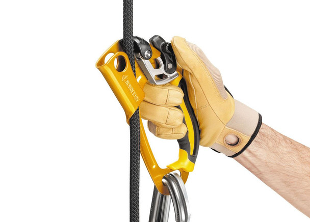 Petzl Ascender, yellow mechanical climbing tool for rope ascension held by a hand wearing a protective glove, with a climbing rope passing through.