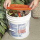 J.Racenstein Lid for 5 and 3 1/2 Gallon Bucket, orange plastic lid shown being placed on a white bucket filled with gardening tools and supplies.