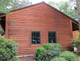 J.Racenstein Tabernacle Harvest Deck and Wood Stain DRP, close-up of a wooden barn exterior with horizontal stained wood siding and two window panes, surrounded by garden plants.