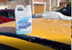 ProTool Foaming Hose End Sprayer, a 2-quart white plastic bottle with a label featuring a blue car and the text 'Shine Up' on it, placed on a yellow car hood covered with foam.