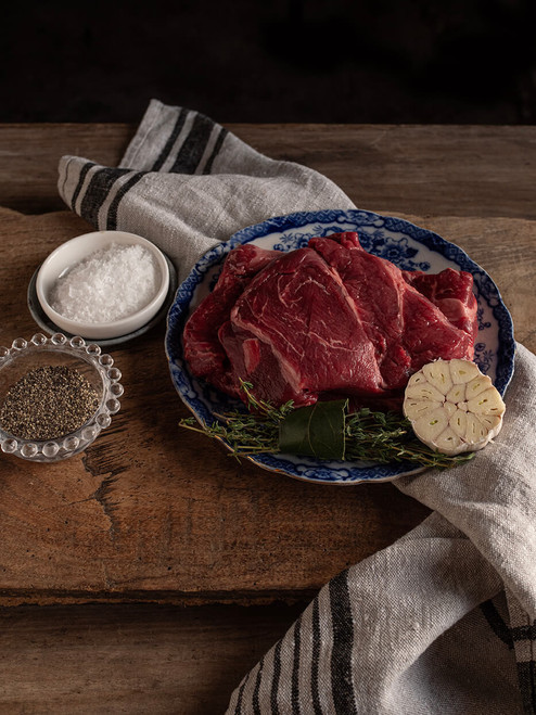 Chuck steak raw on a plate on chopping board with seasoning