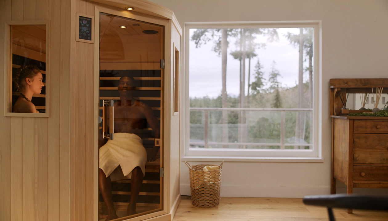 A woman relaxes in a sauna, with a man visible in the background, creating a serene atmosphere. 