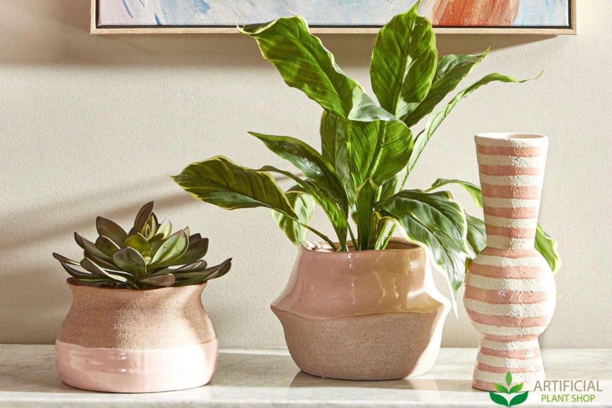 Small artificial plants styled on a marble shelf &mdash; a faux succulent and a leafy green in blush pots