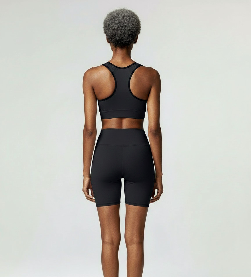 Back view of a model wearing the Anuri Powerform Padded Sports Bra in Ebony with black contrast trim and matching high-waisted shorts.