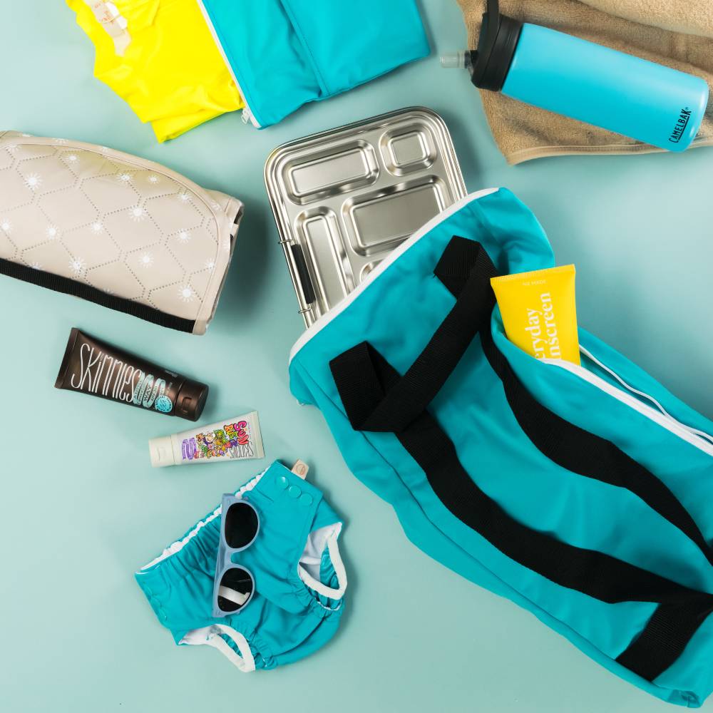 Flat lay - swim nappy aqua, swim bag aqua, sunscreen, double pocket wetbag, drink bottle, lunchbox, sunglasses, swimwear