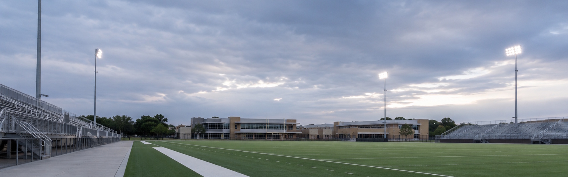 LED sports flood fixtures on galvanized steel poles light an empty high school athletic field for evening football and soccer