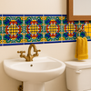 Mexican Tile Tehuacán colorful Talavera tile border in a bathroom wall above a pedestal sink, featuring hand-painted yellow, green, blue, and terracotta scroll motifs with cobalt blue trim