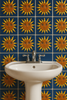 White pedestal sink with chrome faucet against a blue sun-face relief tile wall.