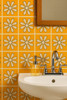 Bathroom wall with orange daisy Talavera tiles behind a white sink and chrome faucet.