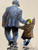 Hopes For The Cup is an original oil painting with a football theme by Alexander Millar. This painting depicts an adult and a child walking away from the viewer. The adult is in a shabby, blue work suit with a flat cap, typical of the attire of working men from the mid 20th century. The adult is carrying an old, leather football under his left arm and has his right arm on the shoulders of the child. The child is wearing a dark green balaclava and  a brown wool coat or a duffle coat. The child is pointing up to the sky, obviously in excited conversation with the adult about his football team's performance.