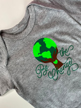 Gray onesie with graphic of hands in Hazelnut EasyWeed Heat Transfer Material holding up the Earth in Green and Fluorescent Green EasyWeed Heat Transfer Material, designed to also resemble a tree. Surrounding the graphic reads, " Be the Change" in a script type font in EasyWeed Green.